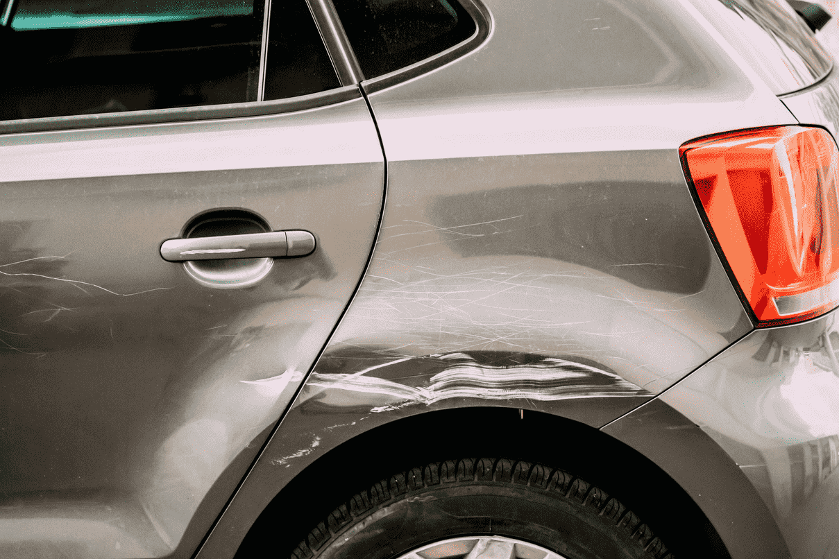 Beschadigde zijkant van auto met krassen en deuk, relevant voor autoverzekering.