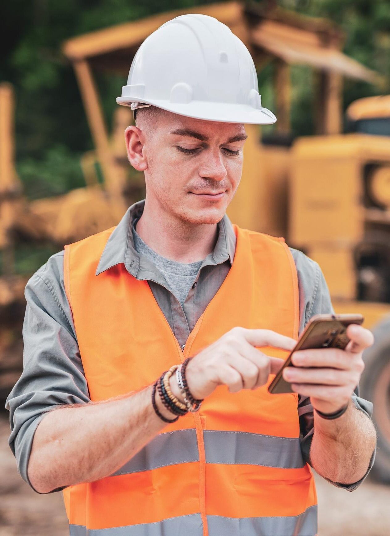 Ondernemer met helm en veiligheidsvest gebruikt smartphone, passend bij verzekeringsadvies voor ondernemingen.