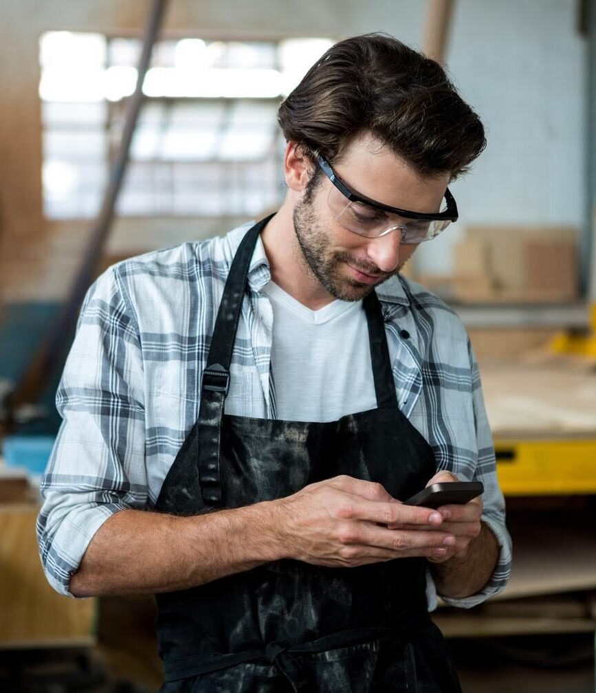 Ondernemer in werkplaats bekijkt verzekeringsopties op zijn smartphone.