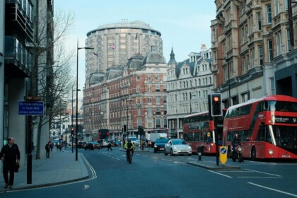 Straatbeeld in Londen met rode dubbeldekkers, klassieke architectuur en Britse vlag – bestemming waarvoor vanaf april 2025 een ETA vereist is.
