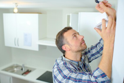 Man installeert een koolmonoxidemelder aan het plafond in een witte keuken.