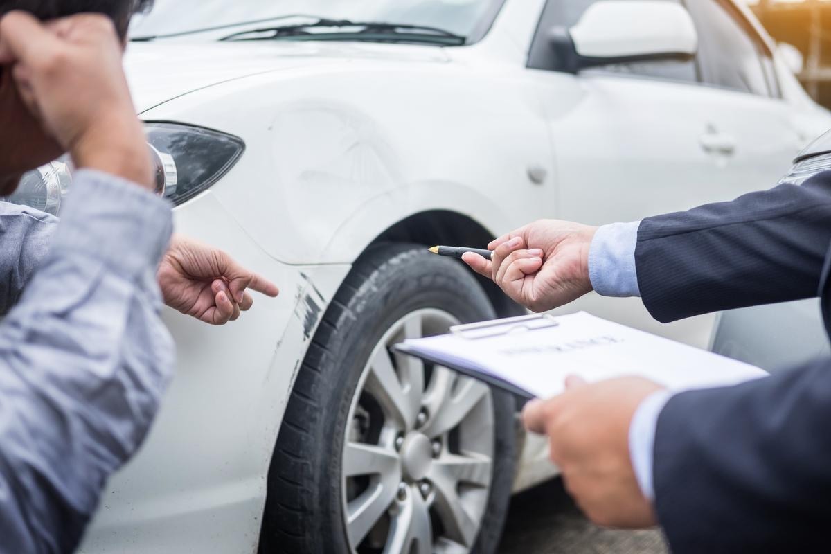 Schade-expert en bestuurder inspecteren autoschade en vullen Europees schadeformulier in voor verzekering.