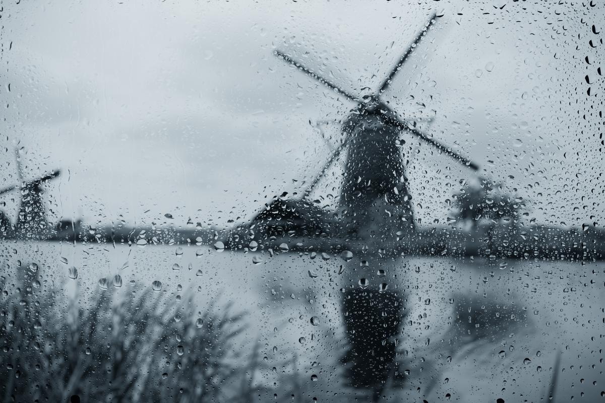 Windmolen in regenachtig landschap gezien door een nat raam, passend bij stormschadepreventie in Nederland.